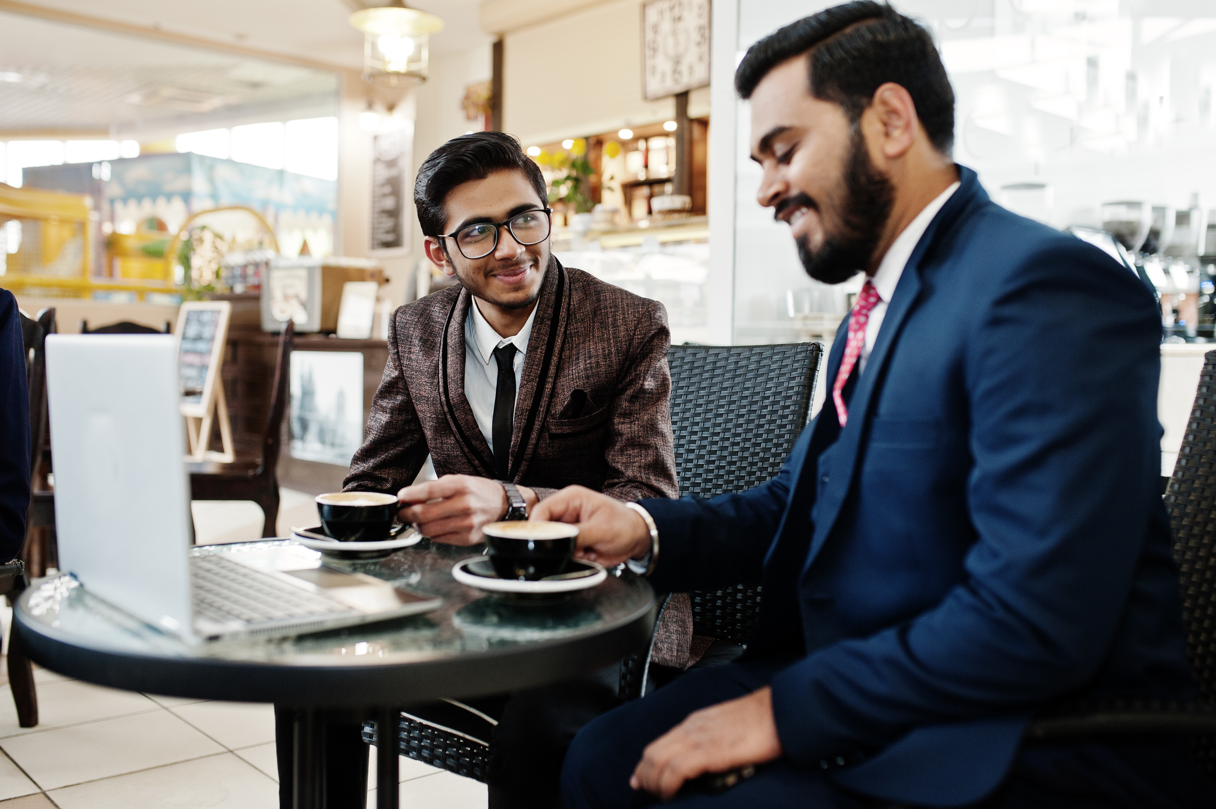 two-indian-business-man-suits-sitting-office-cafe-looking-laptop-drinking-coffee.jpg